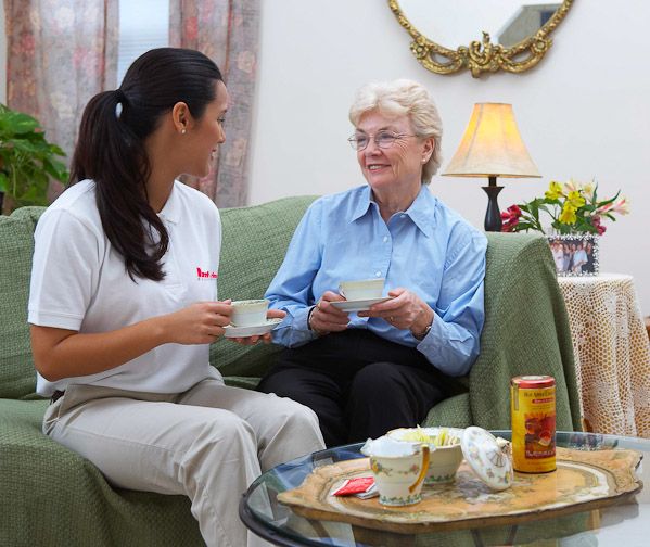 A live-in caregiver having tea with an older woman in her living room
