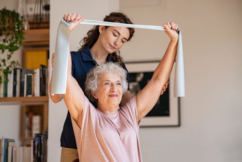 A caregiver guiding an older woman through gentle exercises at home