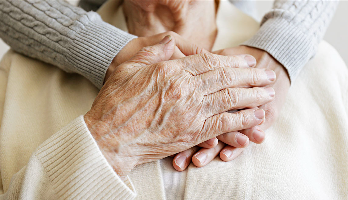 Hands gently holding elderly person's hands in comfort
