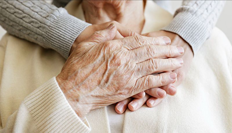Hands gently holding an older person's hands in comfort at home